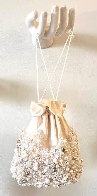 Inspired by four unforgettable days spent sailing through the emerald waters of Ha Long Bay in Vietnam, this elegant reticule captures the quiet beauty of the sea. Some of the pearls were sourced from a small floating water village, giving each piece a meaningful connection the place that inspired it.  

Hand-beaded pearls cascade across softy ivory satin, forming  a richly textured base that shimmers with every movement.  The delicate drawstring silhouette allows the reticule to drape from the wrist.   
